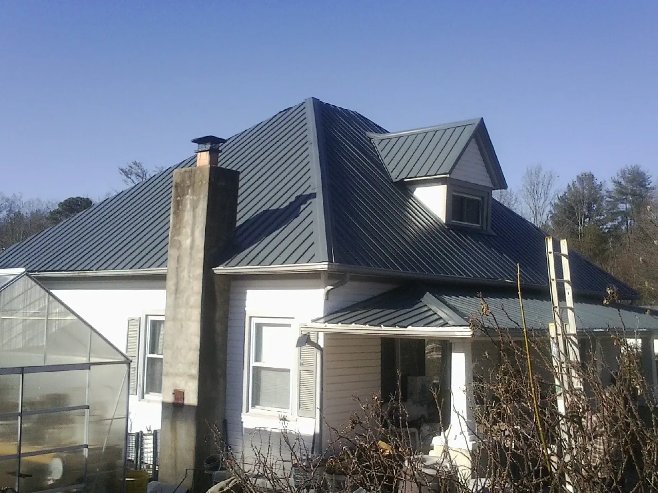 Dark blue standing seam metal roof on a white farmhouse with dormer — Slate & Tile Roof Repair by Roofing Brothers in New Germany