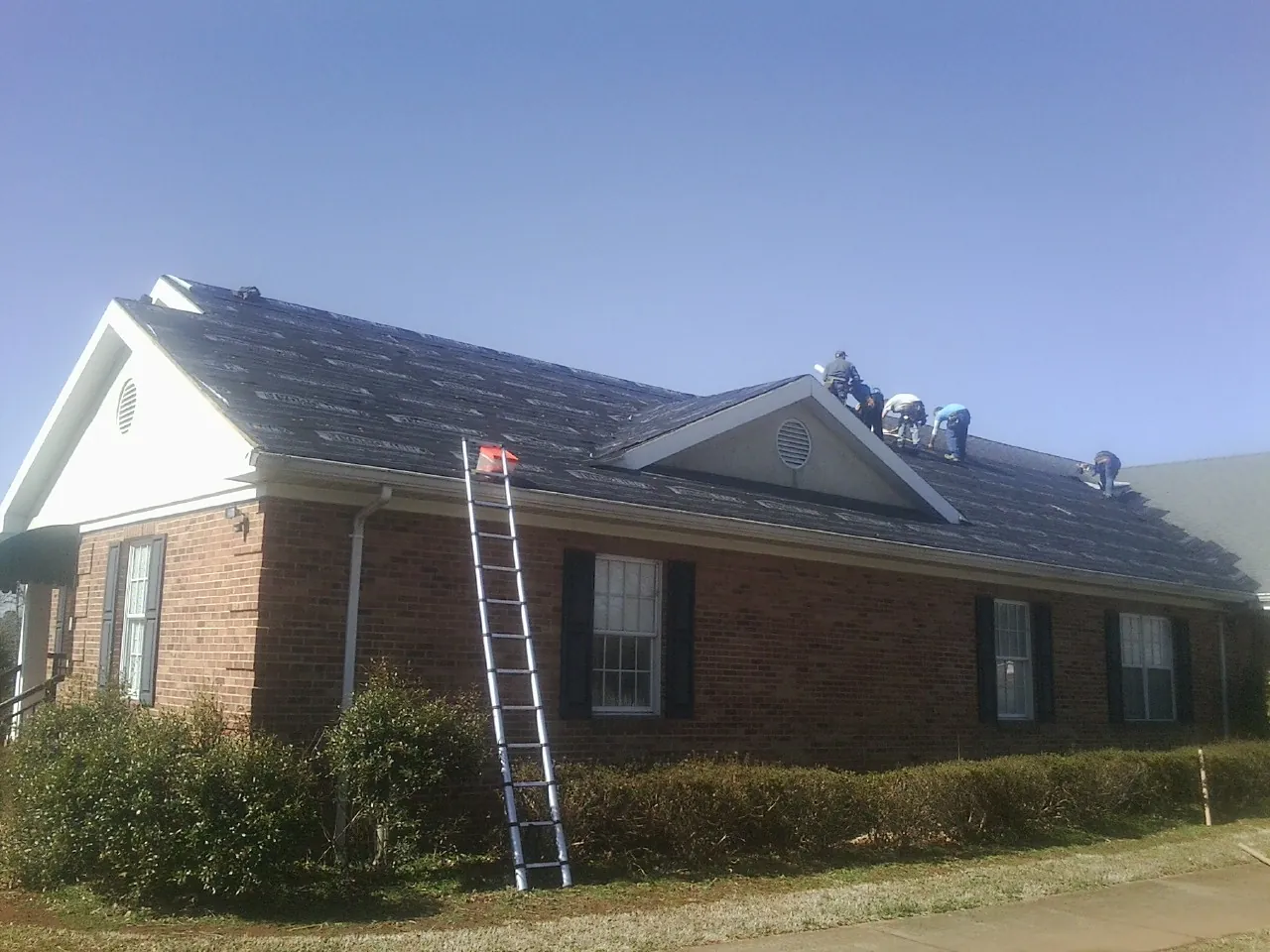 Crew tearing shingles off a brick ranch roof with a ladder set — Metal Roof Repair work by our crew in New Germany
