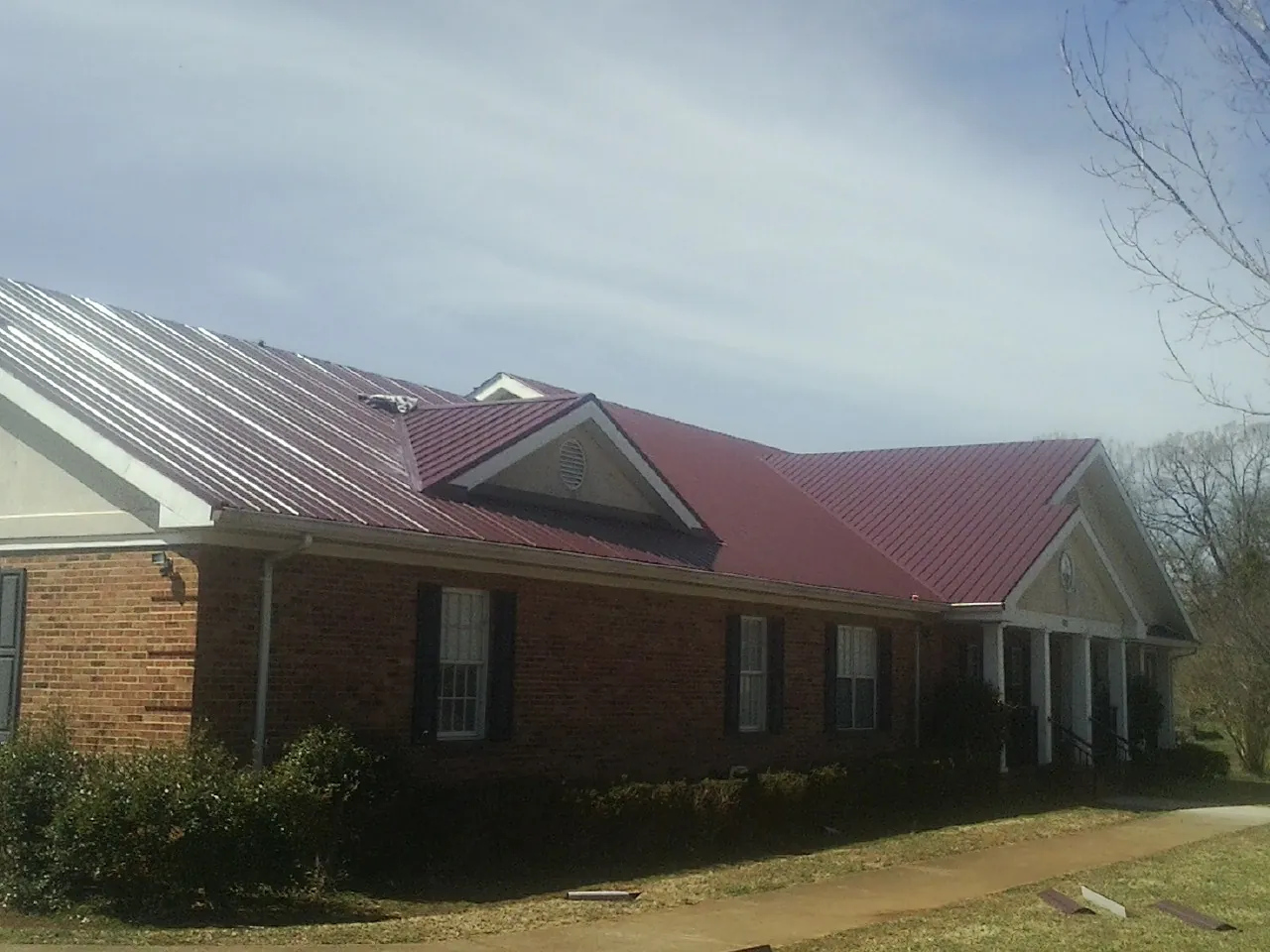 Red metal roof with gabled entries on a long brick building, from a Hail Damage Roof Repair job in New Germany