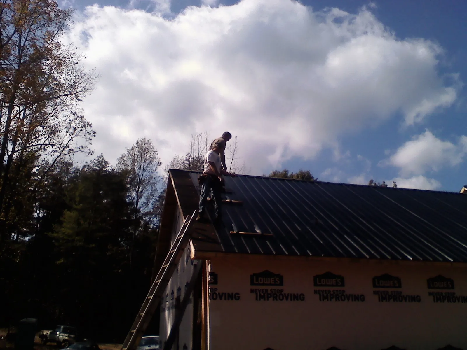 Roofer fastening dark metal panels high against a cloudy sky, from a Roof Inspection job in New Germany