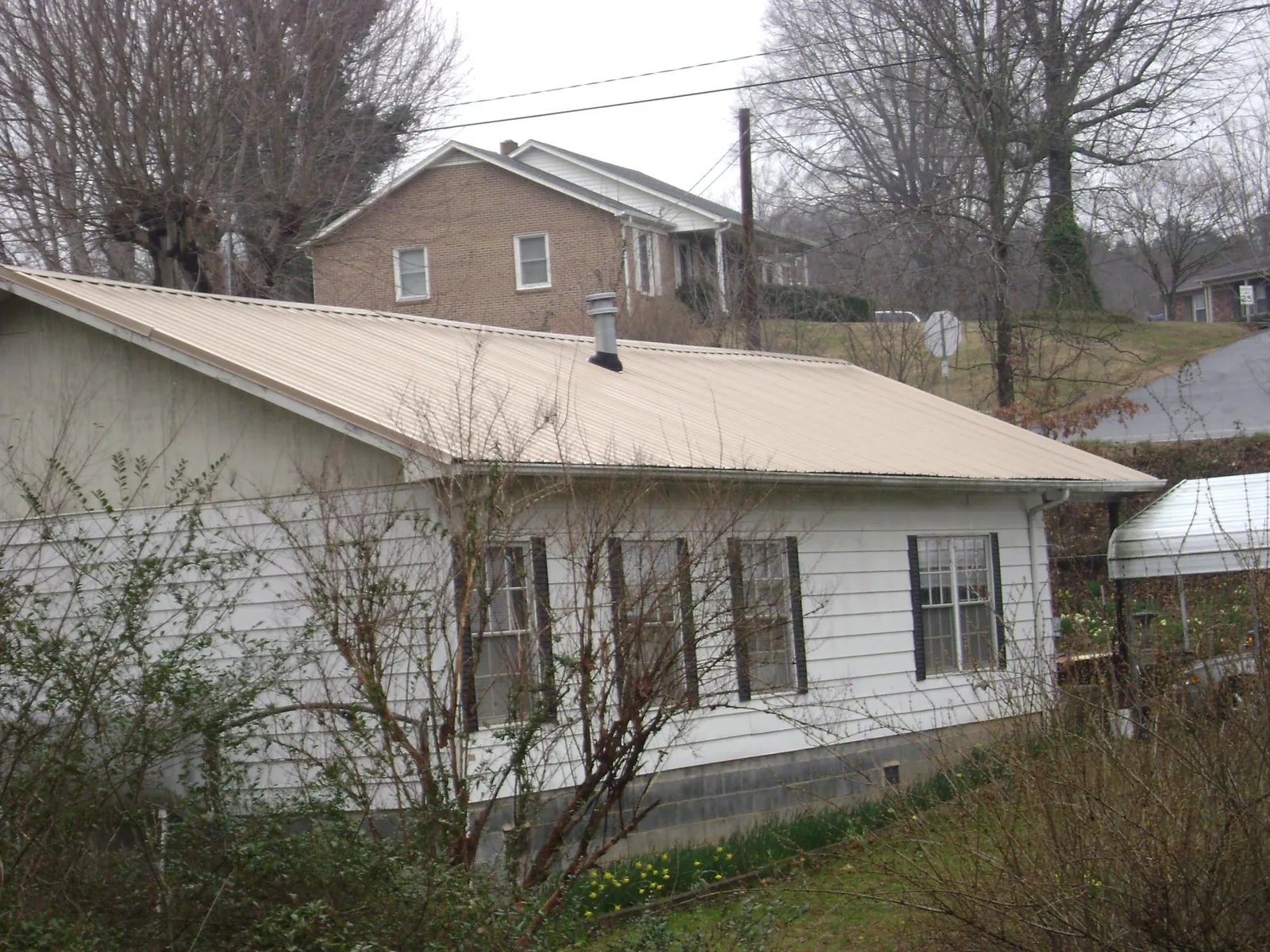 Tan metal roof on a white sided house set into a hillside — Commercial Roofing by Roofing Brothers in New Germany